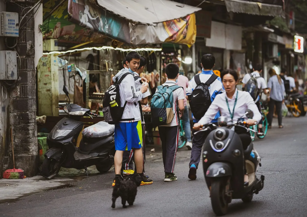 A busy Chengdu side street with schoolkids, a scooter, and small shops — everyday street life, not a tourist lane
