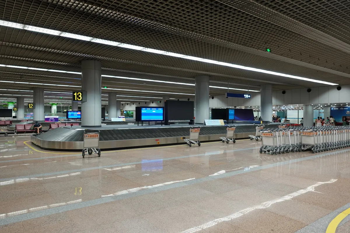 An empty baggage claim hall with carousels and luggage carts at Beijing Capital Airport