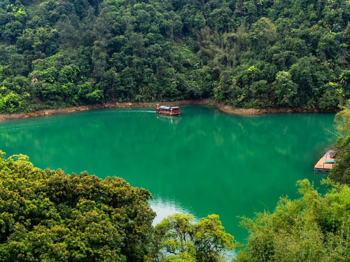 A small red tour boat crossing the emerald-green water of Baofeng Lake, ringed by forest
