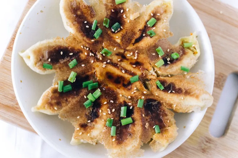 Golden pan-fried dumplings with crisp bottoms arranged in a circle, garnished with scallion