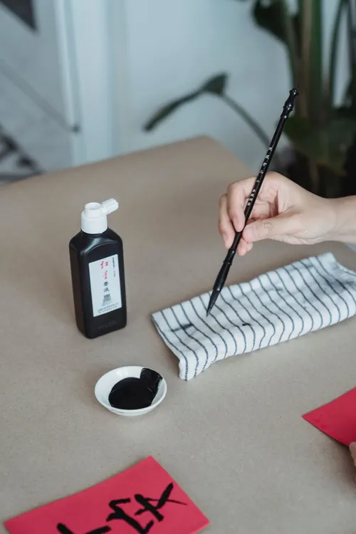 A hand practicing Chinese calligraphy with a brush and ink on paper