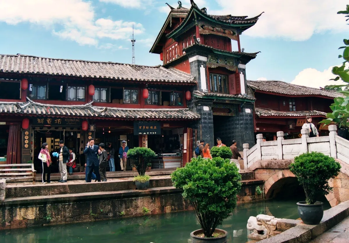 A stone footbridge over a canal lined with traditional Naxi buildings in Lijiang Old Town, daytime