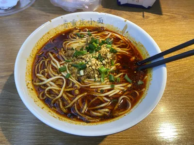 A bowl labeled Chongqing xiaomian with noodles in dark chili oil broth and peanuts