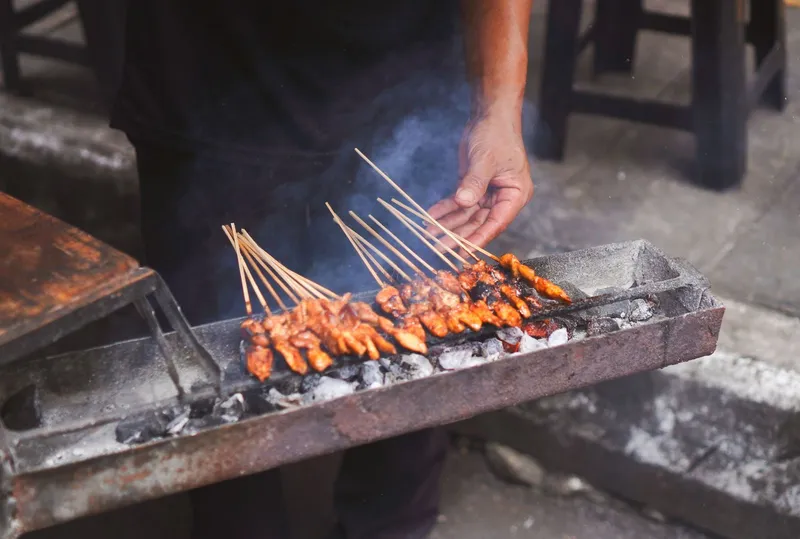 Skewers grilling over charcoal with smoke rising, a hand tending the fire
