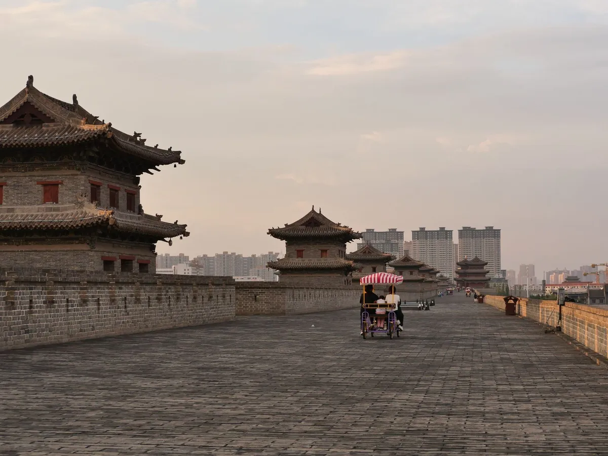 Pedal-cart riders on the wide brick top of Xi'an's City Wall at dusk, watchtowers ahead