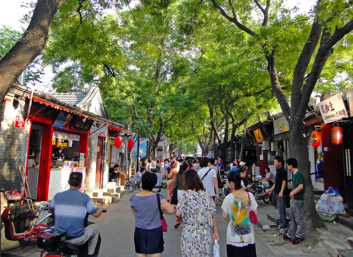 A crowded pedestrian hutong street in Beijing lined with shops and lanterns