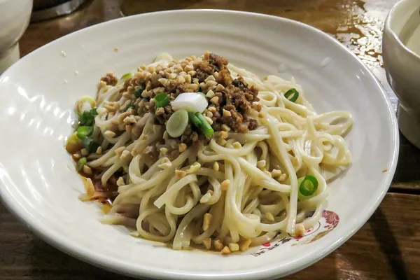 A bowl of dan dan noodles topped with minced pork, peanuts, and scallions in Chengdu