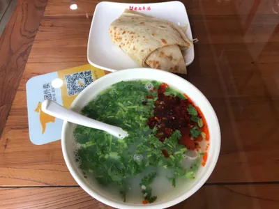 A bowl of lamb offal soup topped with cilantro and chili oil, served with a folded flatbread