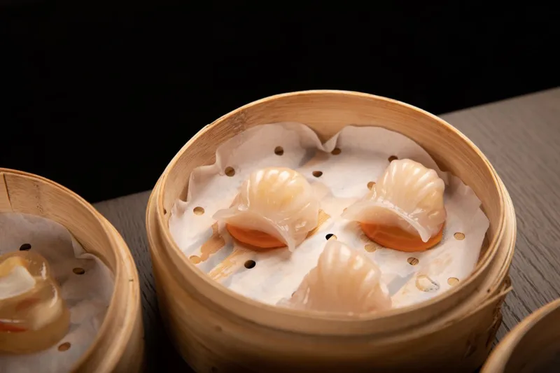 Three pleated translucent har gow shrimp dumplings in a bamboo steamer basket