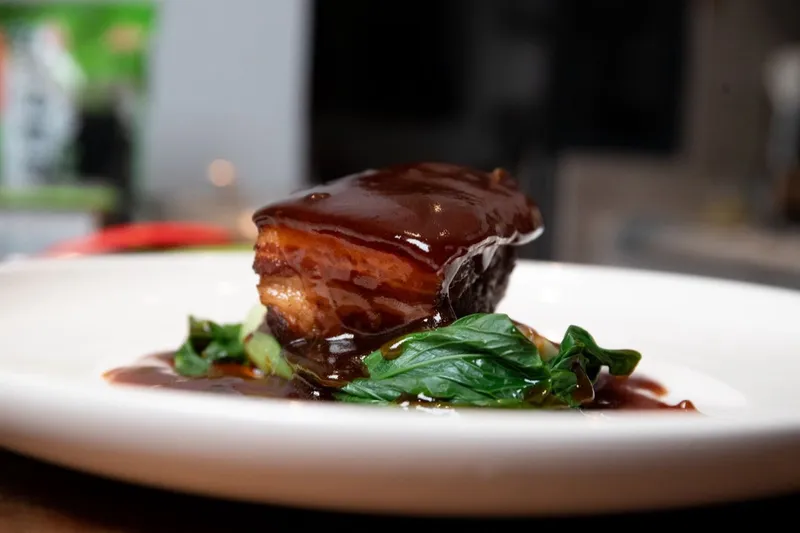 A glazed square of braised Dongpo pork belly with sauce over greens