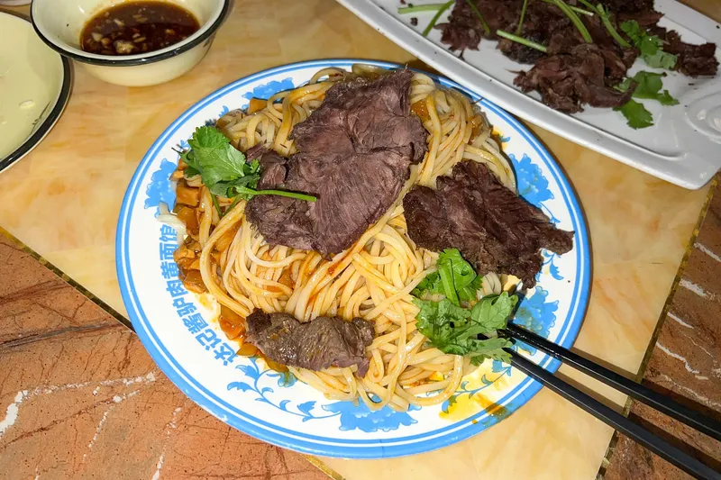 A plate of yellow hand-pulled noodles topped with sliced braised donkey meat and cilantro
