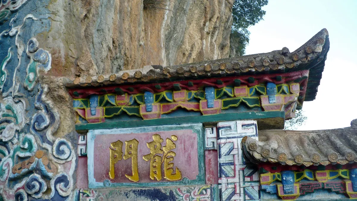 The carved stone Dragon Gate archway set into the cliff face at Western Hills, Kunming, with gilded characters reading 'Dragon Gate'