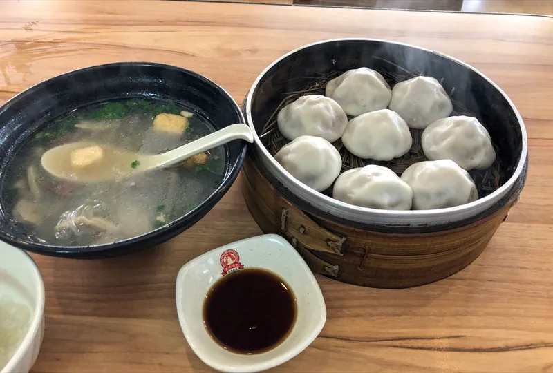 A bowl of duck blood and vermicelli soup beside a steamer basket of soup-filled buns