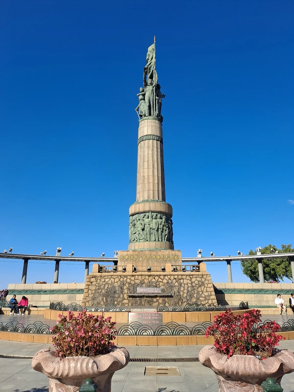 A tall stone column topped with bronze statues of workers holding a flag, the Harbin Flood Control Monument