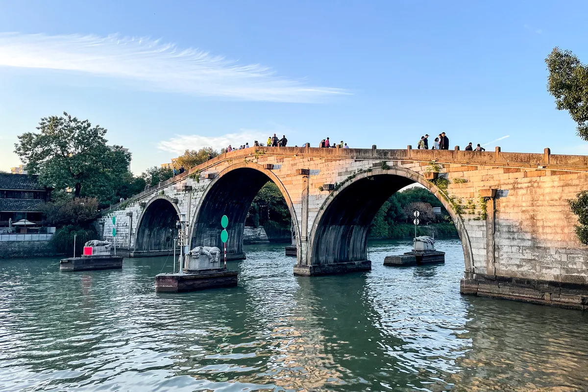 The stone multi-arch Gongchen Bridge over the Grand Canal with pedestrians crossing