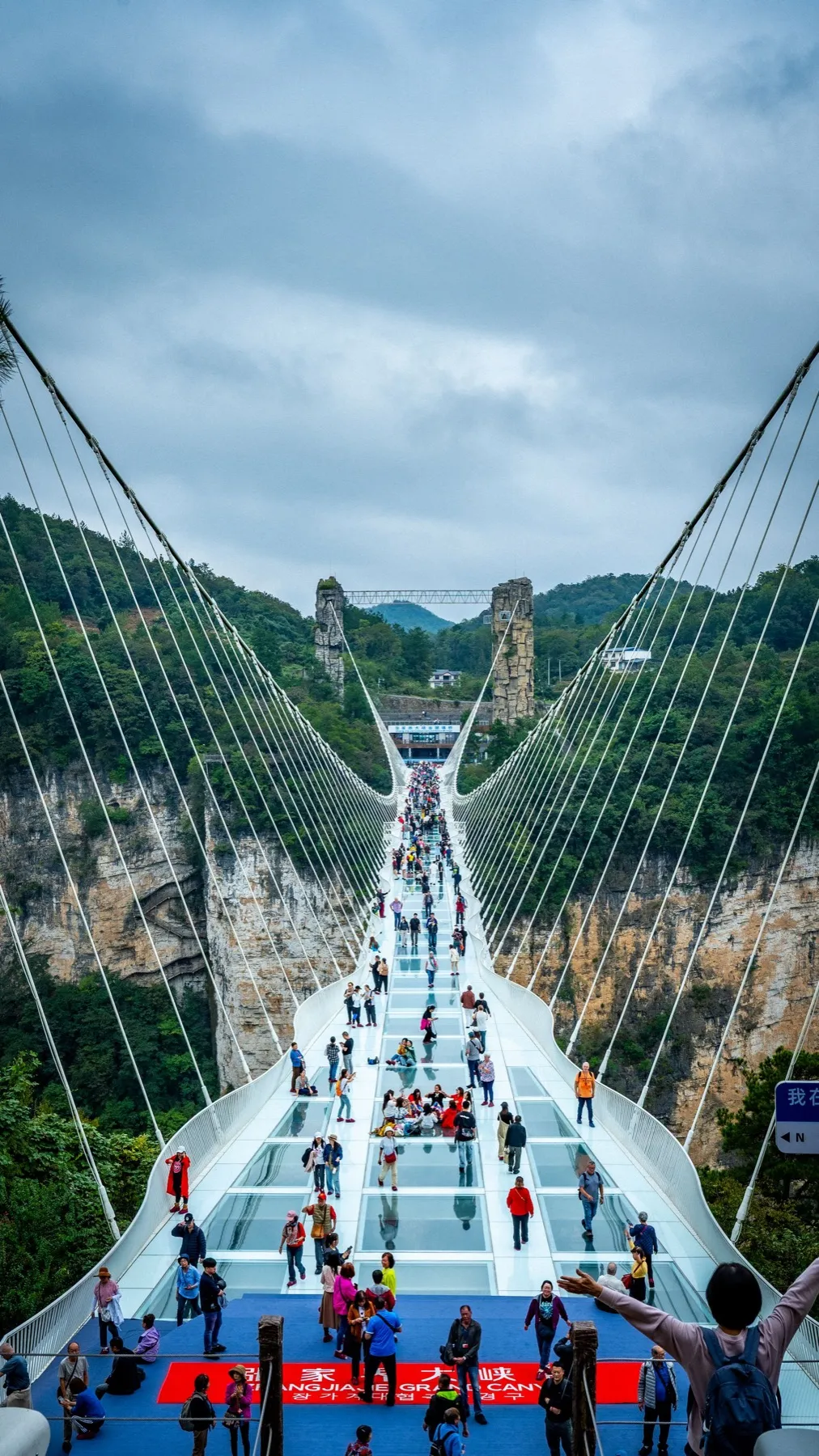 Tourists walking across the glass floor of the Zhangjiajie Grand Canyon Glass Bridge above a forested gorge