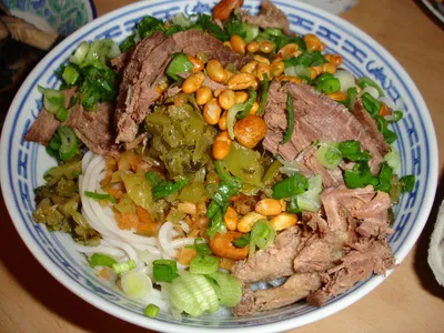 A bowl of Guilin rice noodles topped with braised meat, peanuts, and pickled vegetables
