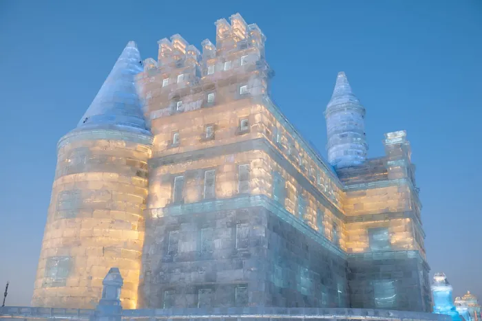 An illuminated ice castle with turrets glowing gold and blue at Harbin Ice and Snow World at dusk