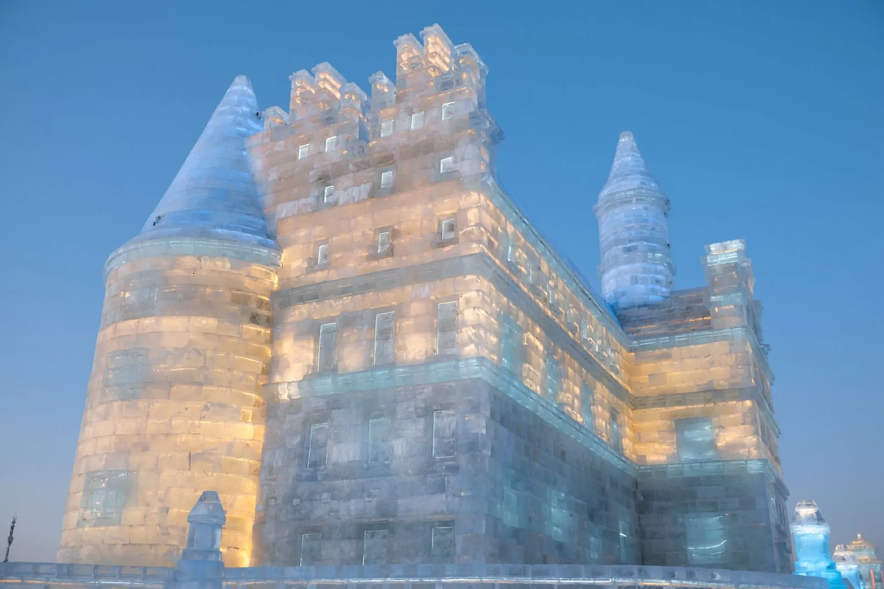 An illuminated ice castle with turrets glowing gold and blue at Harbin Ice and Snow World at dusk