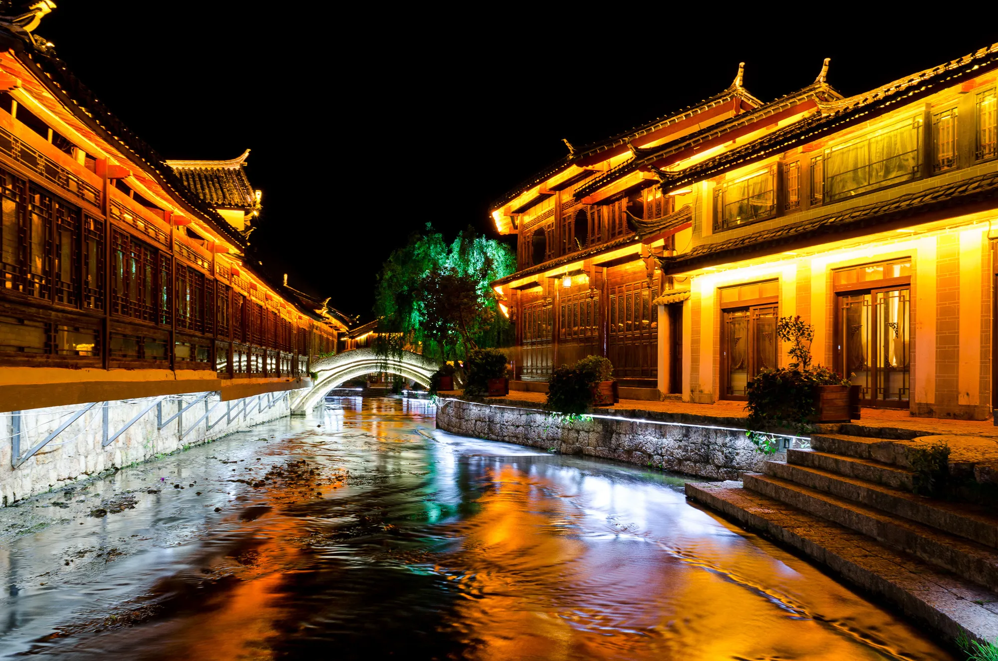 Lijiang Old Town's lantern-lit canal and Naxi timber buildings reflected in the water at night