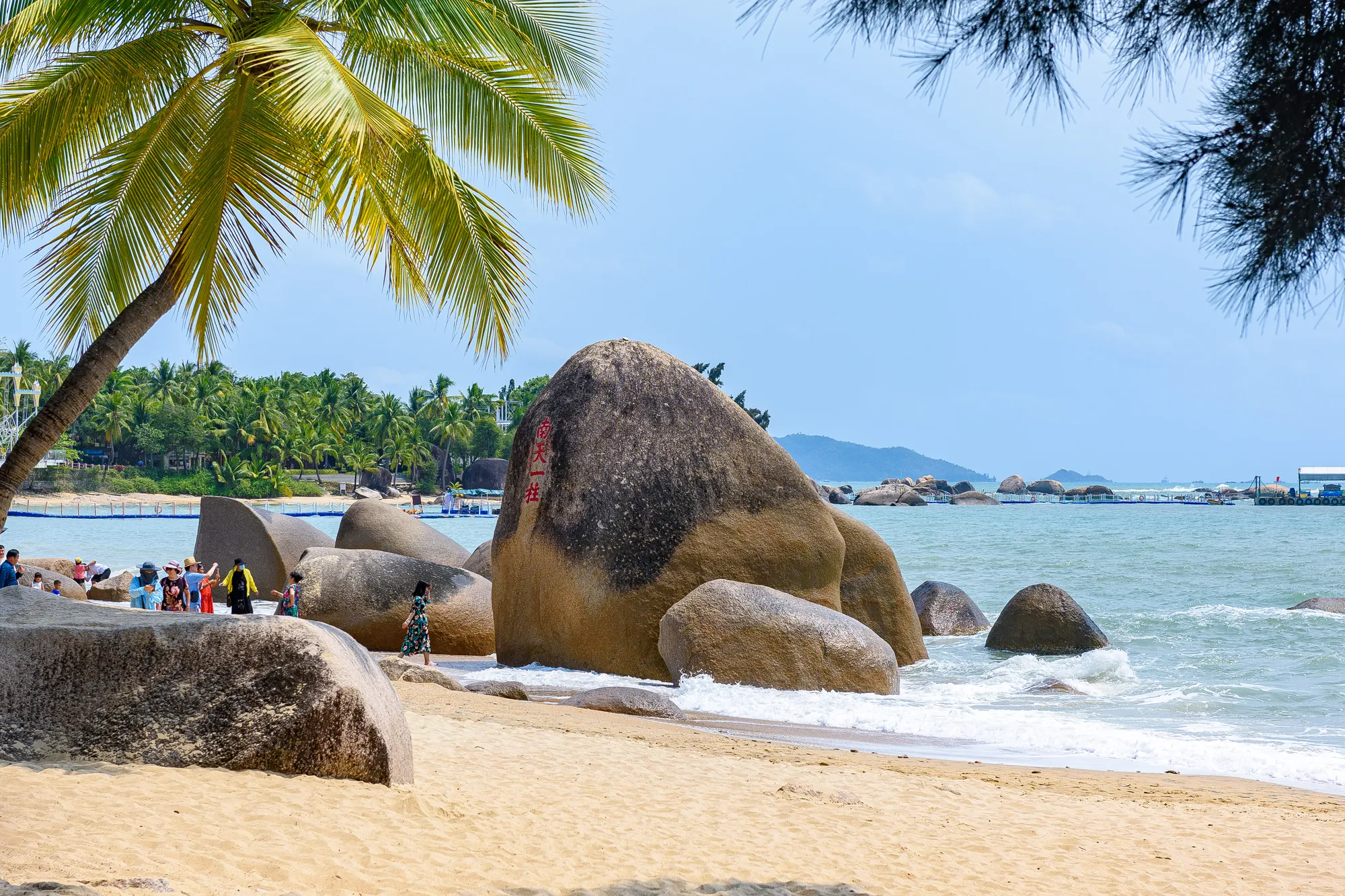 The inscribed Nantian Yizhu boulder on the beach at Tianya Haijiao, framed by a palm tree
