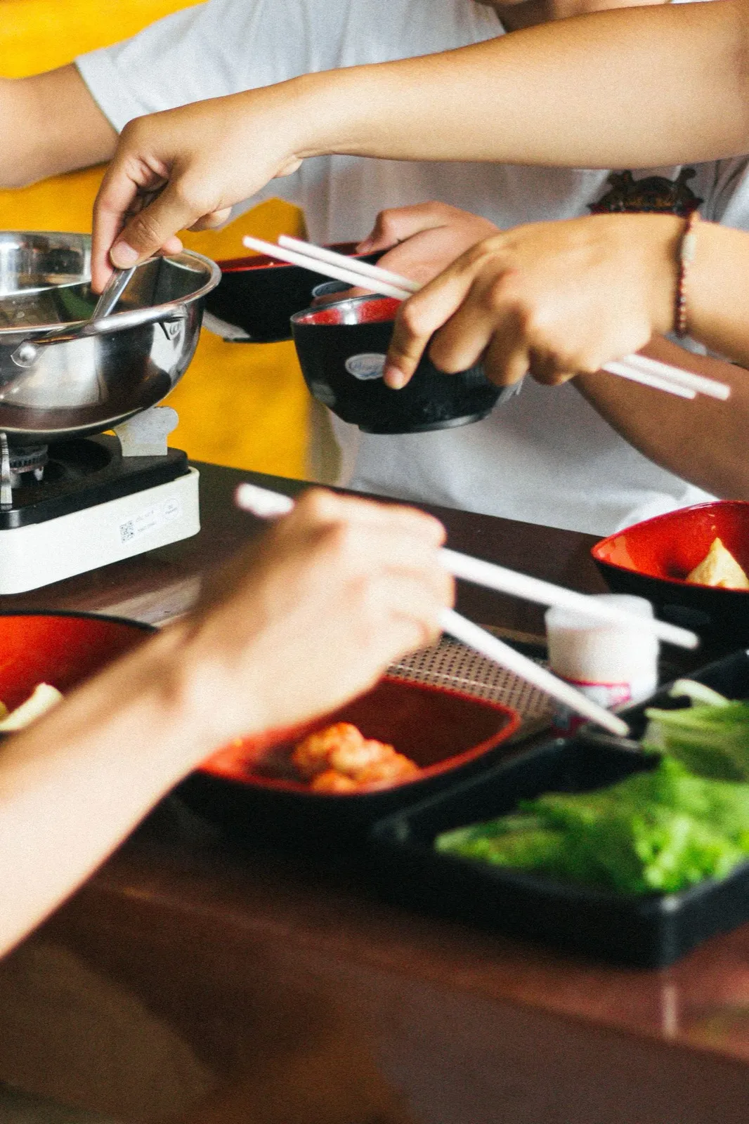 Diners cooking ingredients in a hotpot at a shared restaurant table