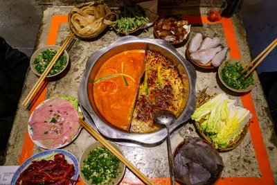 A split Chongqing hotpot with spicy tallow broth surrounded by raw ingredients on ice