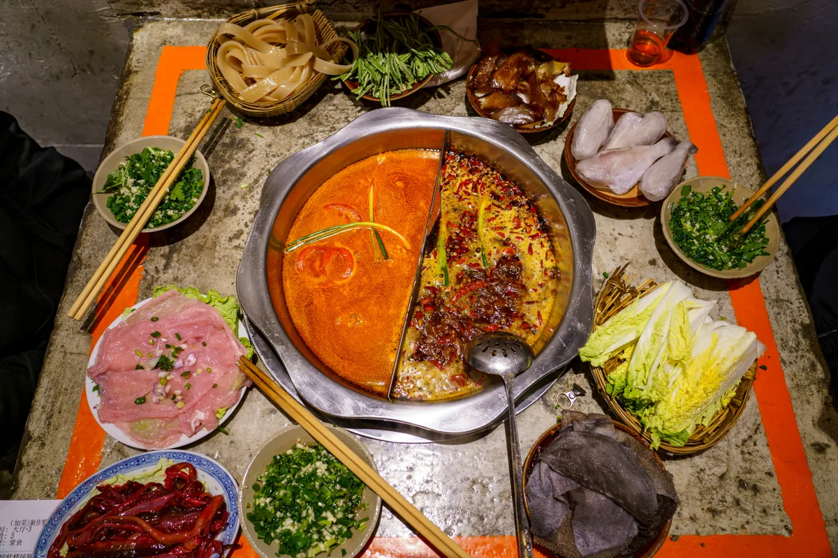 A split Chongqing hotpot with spicy tallow broth surrounded by raw ingredients on ice