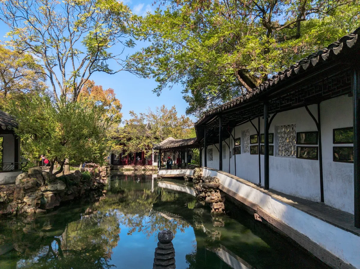 A covered corridor and pond reflecting traditional white-walled pavilions at the Humble Administrator's Garden