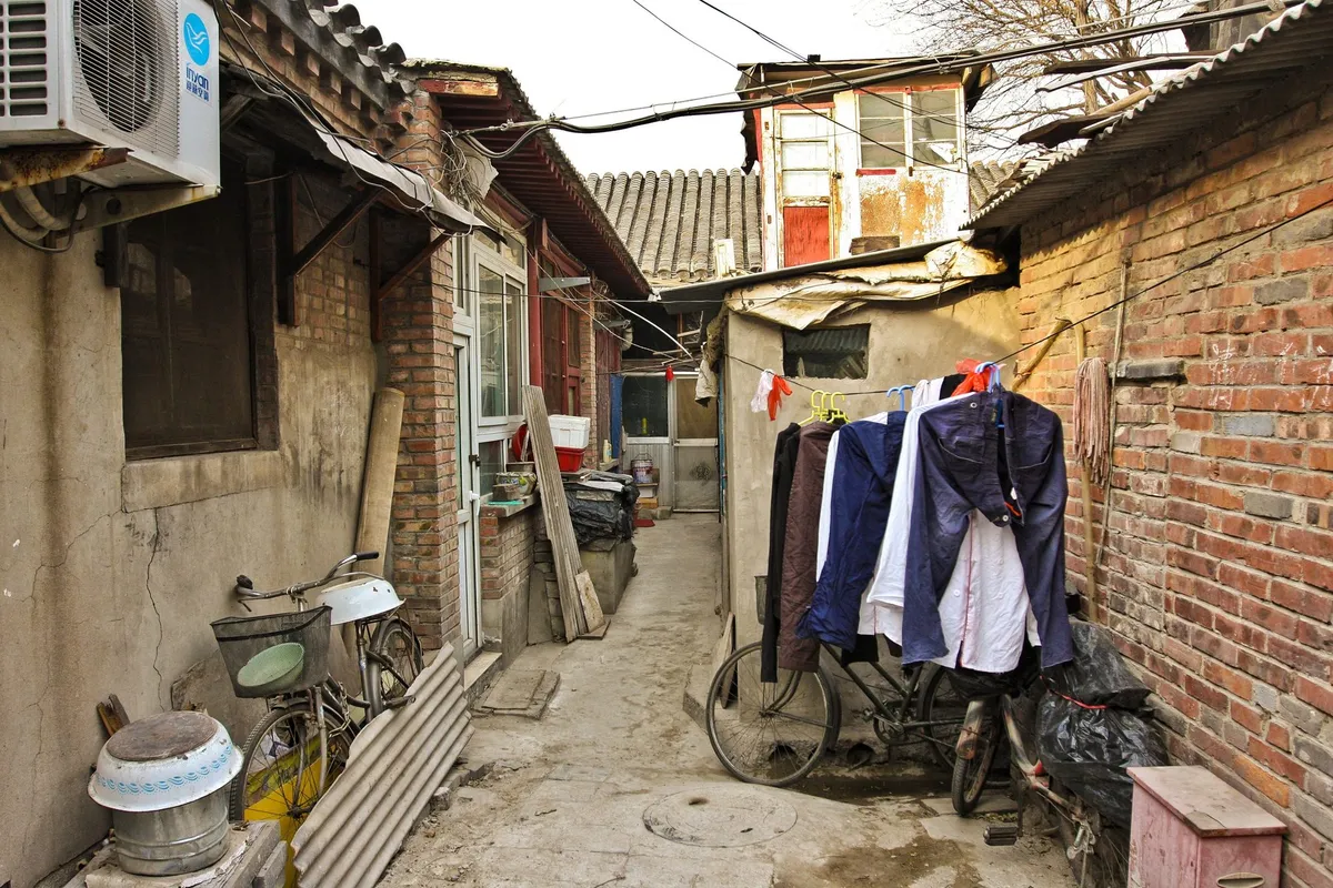 A narrow Beijing hutong alley with brick courtyard walls, a parked bicycle, and laundry hung out to dry