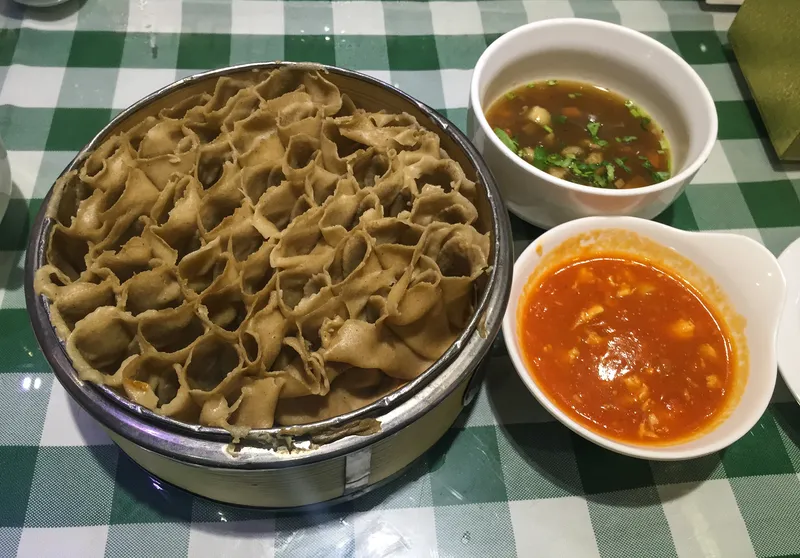 Steamed oat noodle rolls stacked in a honeycomb pattern beside tomato and braised-mutton dipping sauces