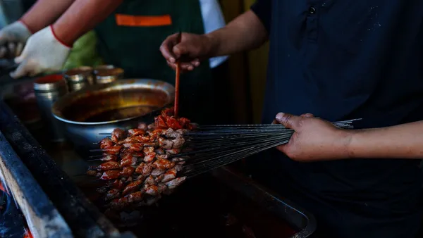 A street vendor saucing bundles of thin lamb skewers over the grill