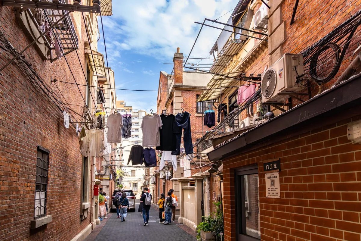 A narrow Shanghai lane between brick lane houses, laundry hanging overhead, residents walking through