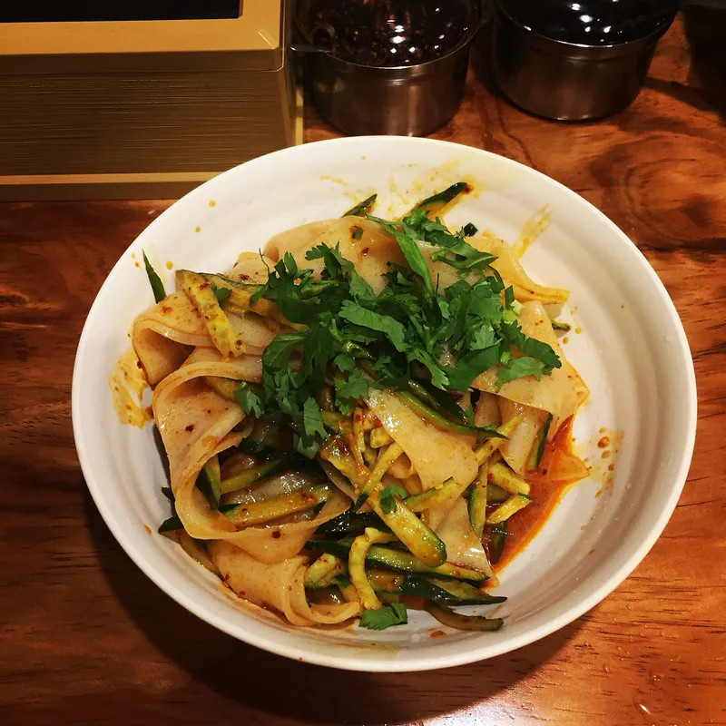 A bowl of cold liangpi noodles tossed with cucumber, cilantro, and chili oil