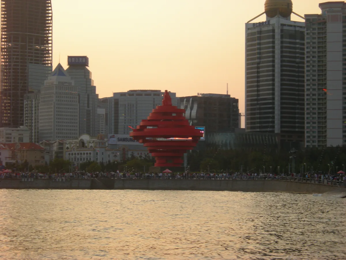 The red spiral 'Wind of May' sculpture at May Fourth Square with the Qingdao skyline behind it