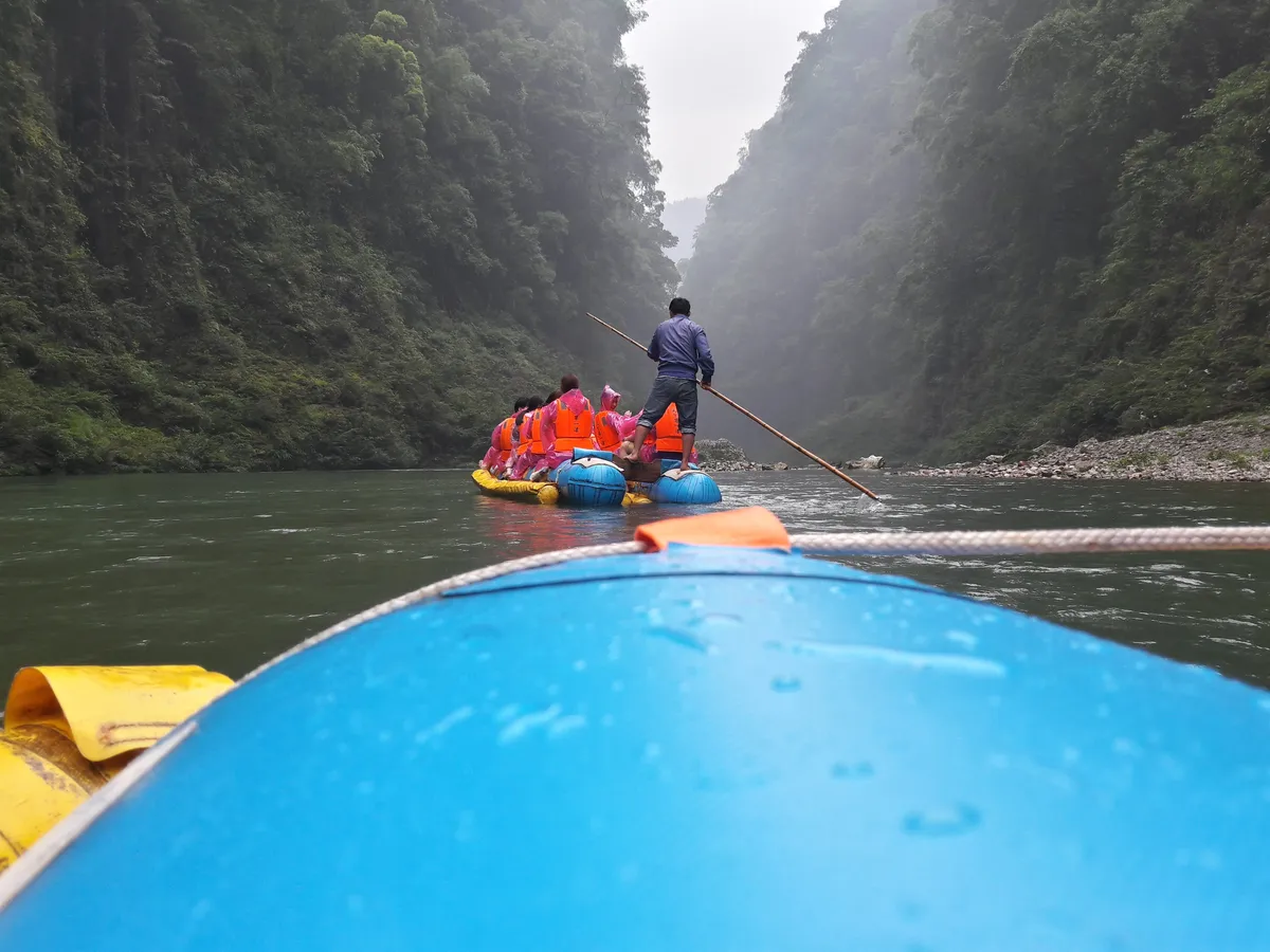 Tourists in life jackets riding a bamboo raft down the forested Mengdong River gorge, poled by a guide