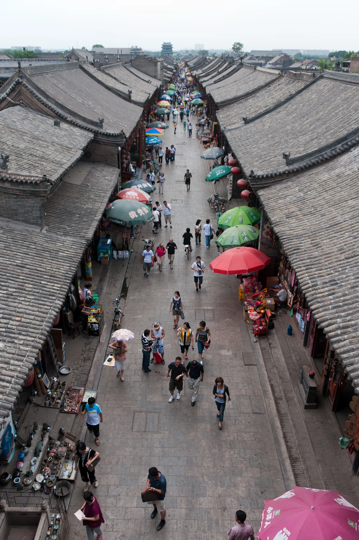 An elevated view down Pingyao's Ming-Qing Street, lined with tiled shopfronts, umbrellas, and the Market Tower in the distance