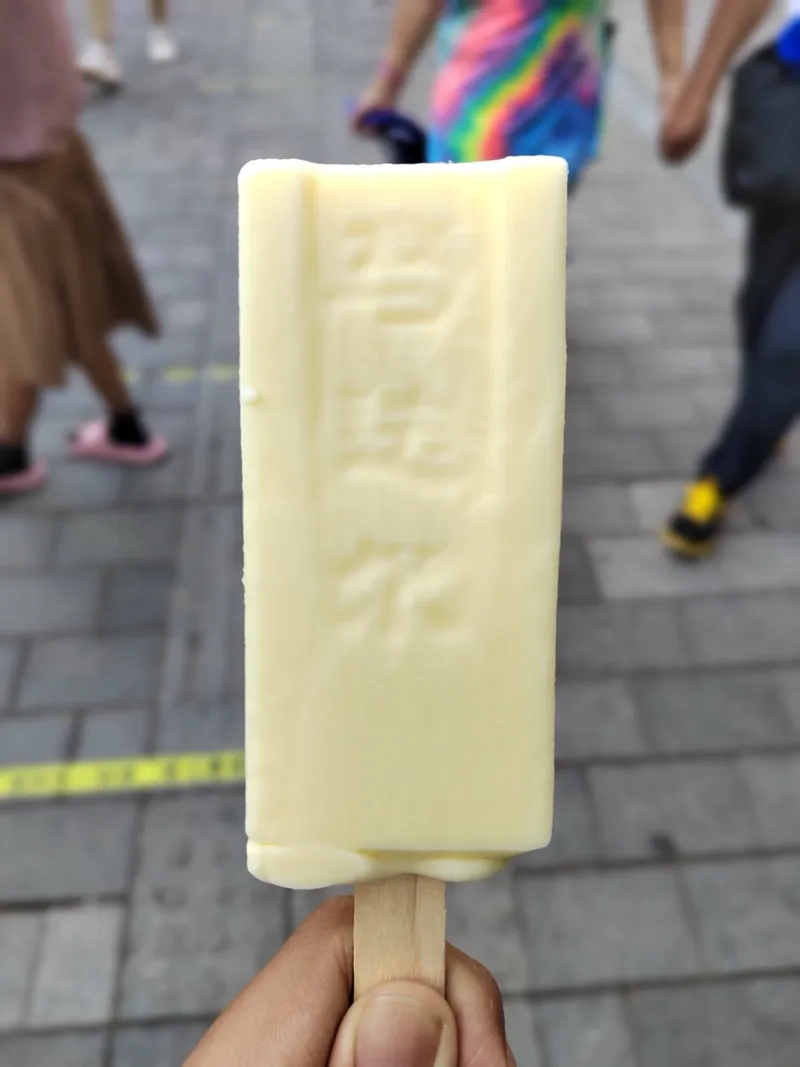 A hand holding a pale yellow Modeler ice cream bar with embossed lettering, Central Street in the background
