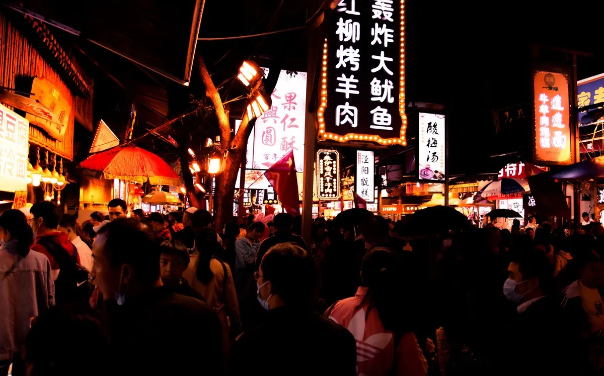 A bustling night scene on Huimin Jie with illuminated food-stall signs and crowds