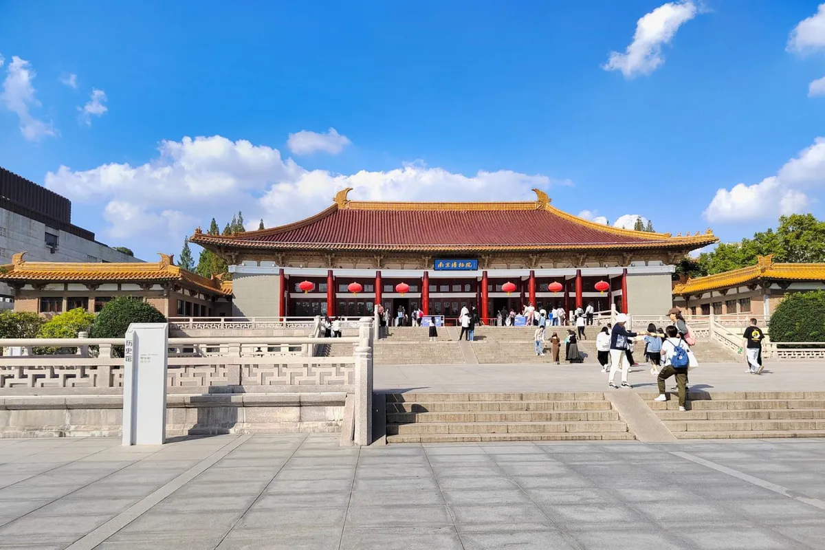 The grand yellow-roofed hall of Nanjing Museum with red lanterns and a plaza of visitors