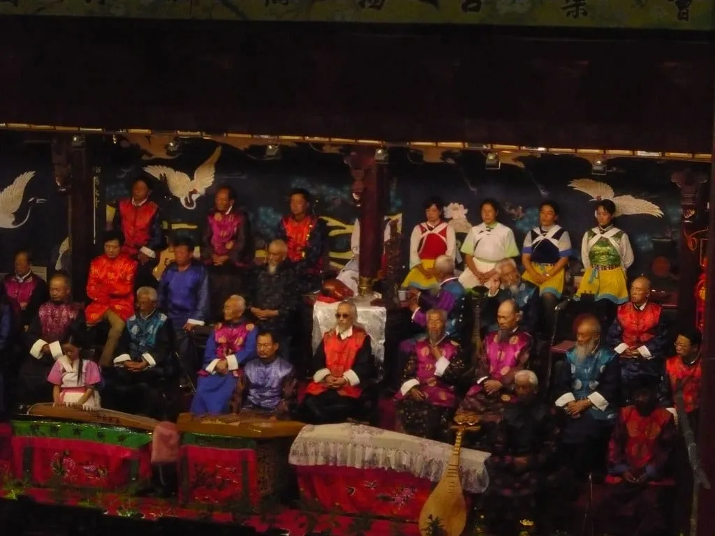Elderly Naxi musicians in formal robes performing traditional instruments on stage in Lijiang