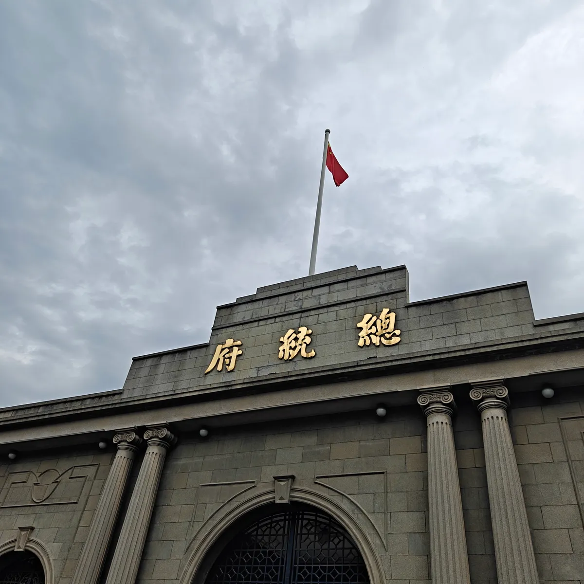 The stone gate of Nanjing's Presidential Palace with gold '總統府' characters and a red flag