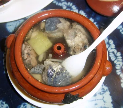 A terracotta steam pot of qiguo ji chicken soup with visible chicken pieces and ginger, the pot's central steam spout visible