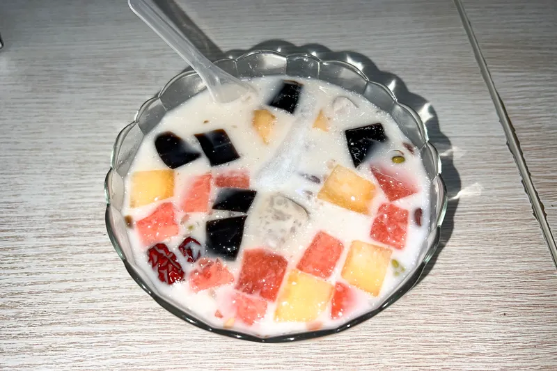 A glass bowl of qingbuliang — coconut milk with colorful fruit, jellies, and red dates