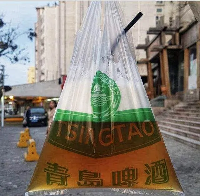 A plastic bag of golden draft Tsingtao beer with a straw, held up against a street backdrop