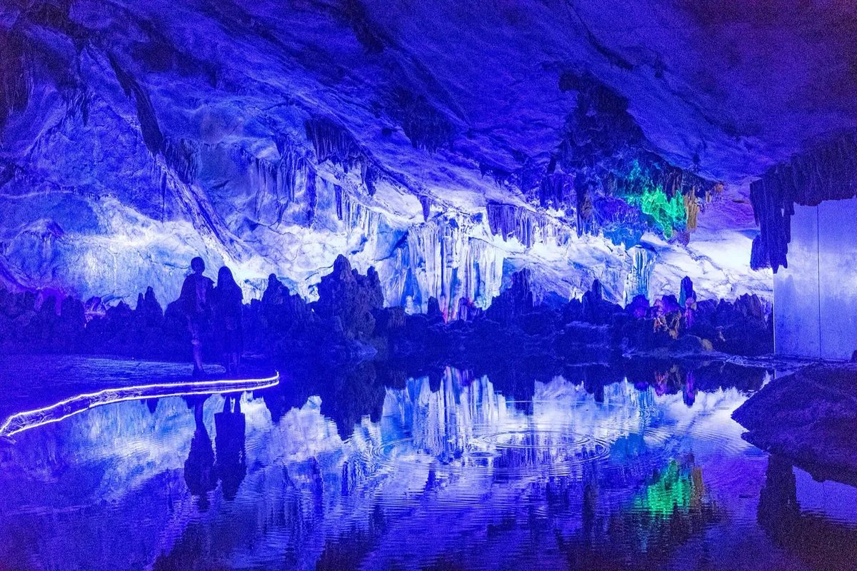 Illuminated blue and green stalactites reflected in a pool inside Reed Flute Cave