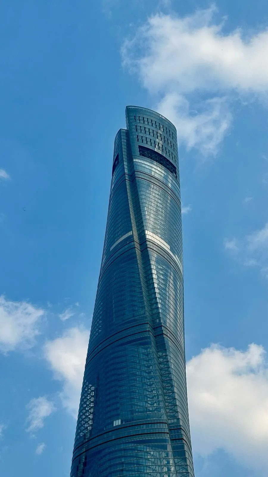 Low-angle view of the twisting glass facade of Shanghai Tower against a blue sky