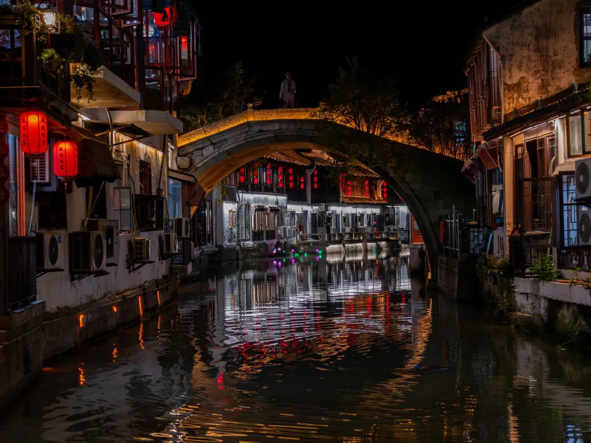 An arched stone bridge over a canal lit up at night on Shantang Street in Suzhou