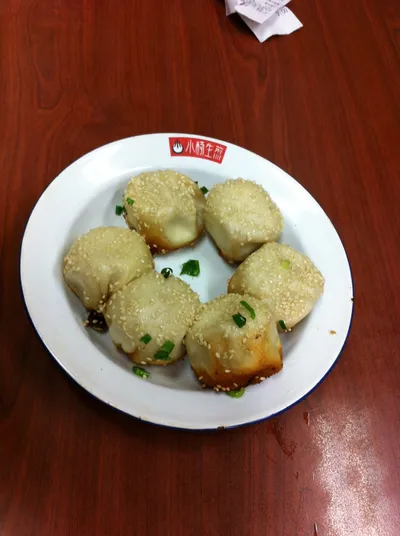 Six sesame-topped shengjianbao pan-fried buns on a plate at Xiao Yang Sheng Jian