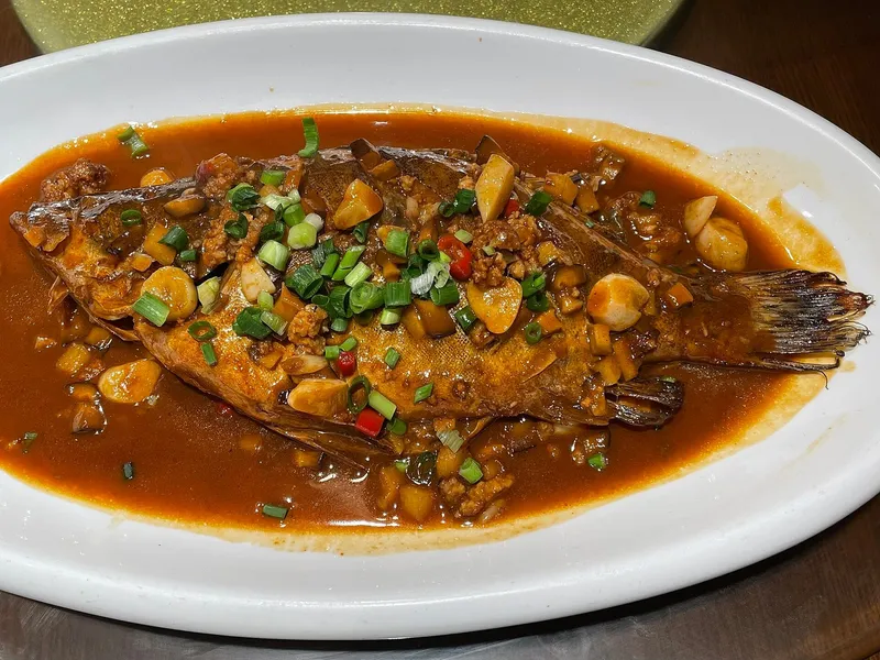 A whole braised stinky mandarin fish in dark sauce topped with scallions